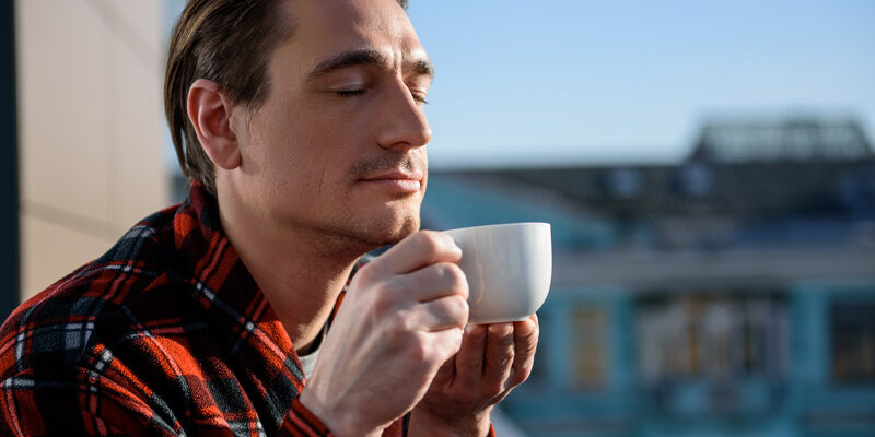 A man standing outside as he smells his cup of coffee
