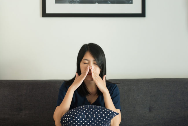 Woman experiencing sinus pain while sitting on her couch
