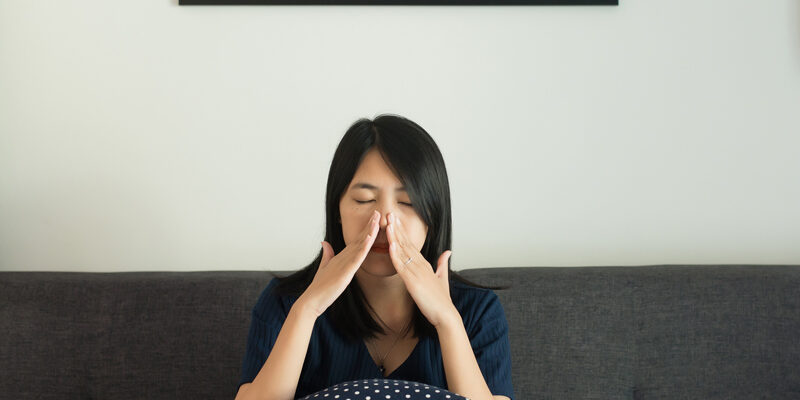 Woman experiencing sinus pain while sitting on her couch