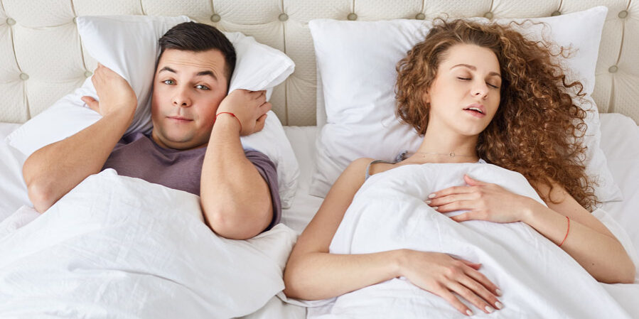 Man covers his ears as the woman next to him snores